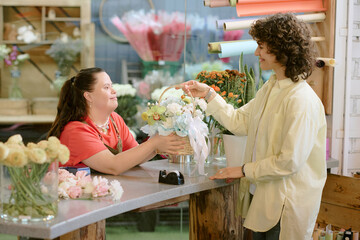 Pretty woman buying flowers in popular flower shop with wonderful florist with down syndrome