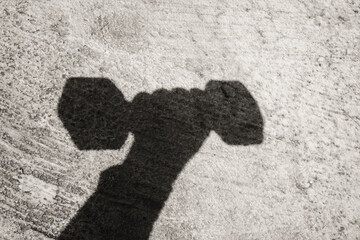 Silhouette of hand holding dumbbell in monochrome. Black and white photo of a hand gesture with a cement wall background. Artwork and Visuals. Negative space. Silhouette photography theme