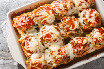 Baked dinner rolls stuffed with meatballs, topped with tomato sauce and sprinkled with cheese close-up in a baking dish on the table. horizontal top view from above