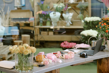 Medium close up of work table of florist with crystal vase, flowers and laptops with satin ribbons on top