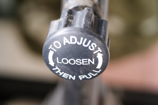 Closeup of a knob on a bicycle frame. The knob is used to adjust the seat height on a bicycle. The knob is black plastic with white text instructions. Bicycle accessories