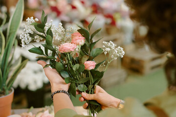 High angle shot of small but elegant bouquet of bush roses, gypsophila and green ruscus in unrecognizable female hands