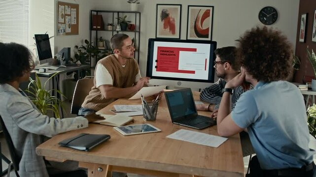 Group of multi-ethnic colleagues discussing project financing during business meeting in modern office, while sitting at table and listening to presentation