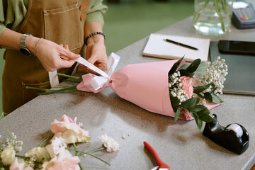 High angle shot of unrecognizable florist teeing bow of satin ribbon to make elegant bouquet better