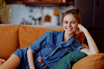 Obraz premium Happy young woman in casual denim shirt relaxing on sofa in cozy living room at home