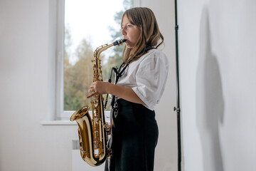 Girl playing, practicing the saxophone, playing a melody on a musical instrument, standing against...