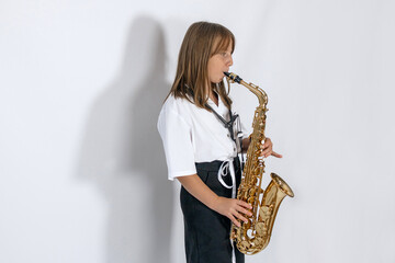 Girl playing, practicing the saxophone, playing a melody on a musical instrument, standing against...
