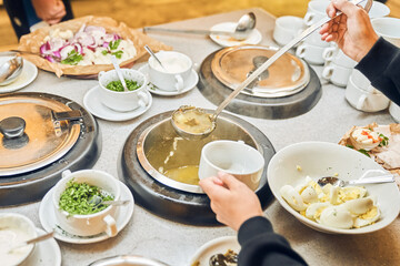 Buffet in the restaurant. Hands put a ladle of liquid soup. A delicious hot dish in cups with a variety of fresh vegetables and tender meat, simmered in a spicy broth. High quality photo