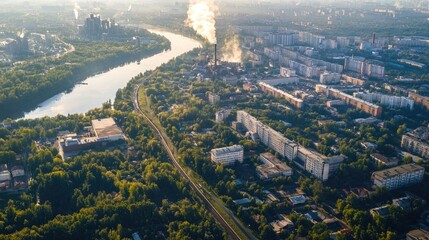 Fototapeta premium Aerial summer cityscape featuring smoky metallurgical plant by river with lush greenery and urban landscape under bright sunshine