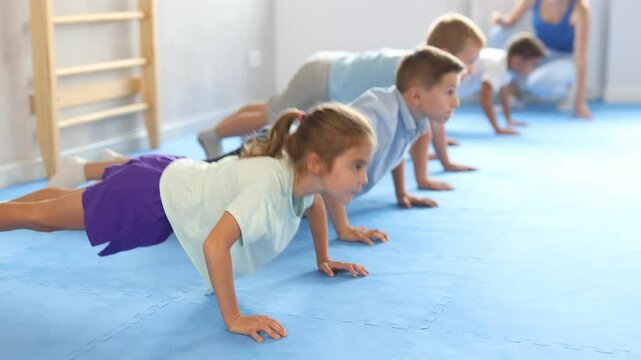 Group of little children doing push-ups on sports mats during a self-defense class in a gym. High quality 4k footage