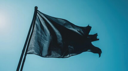 Close up of a tattered black flag waving against a clear blue sky symbolizing rebellion and defiance in a striking contrast
