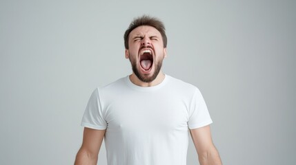 Obraz premium Young man expressing intense emotion with open mouth against plain background, showing frustration and energy
