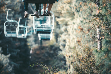 A couple's feet dangle from a chairlift high above a lush, green mountainside in Yunnan, China. The view evokes the beauty of Dali's natural landscape.