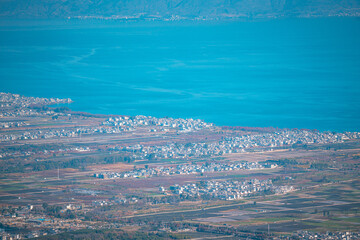 Here is a description and keywords based on your requirements:

**Image Description:**

Aerial view of a vast, turquoise lake meeting a sprawling town in Yunnan, China. The Dali landscape unfolds, sho