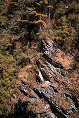 Sun-drenched rocky hillside in Yunnan, China, near Dali. Lush vegetation clings to the steep, textured slopes.  A small waterfall is partially visible.