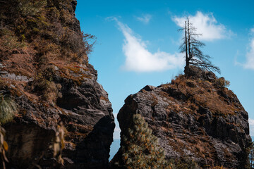 Fototapeta premium A dramatic cleft in the Yunnan, China mountains reveals a vibrant blue sky and a lone, tenacious tree clinging to the rock face. The Dali landscape is stark yet beautiful.