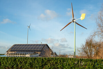 Two windmills and solar battery on the roof of the house against the background of blue sky with...