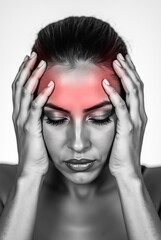Fototapeta premium A woman is visibly struggling with a headache, clutching her forehead with both hands. Her facial expression conveys discomfort, set against a simple background.