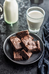 Homemade chocolate brownies on plate and glass of milk on black table.