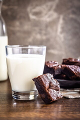 Homemade chocolate brownies and glass of milk on wooden table.