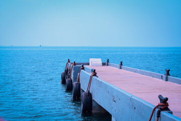 Fototapeta premium A Concrete Pier Extending Into The Sea Under a Clear Sky With Equipped With Black Rubber Bumpers Tied With Ropes.