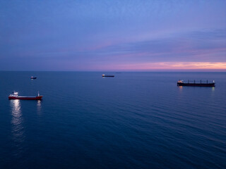 Fototapeta premium Serene sunset over calm sea with cargo ships illuminated by golden light, creating a tranquil maritime atmosphere