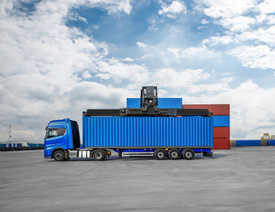 A blue semi truck is parked in front of a stack of blue shipping containers