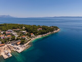 Fototapeta premium Aerial view of a coastal village with lush greenery and clear blue waters. Bol, Croatia