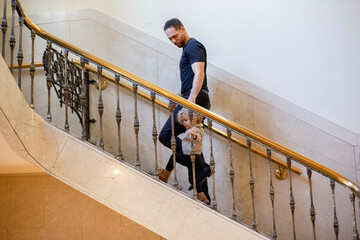 Adult man and young girl holding hands while descending a grand staircase with ornate railing. Cleveland, Ohio, USA