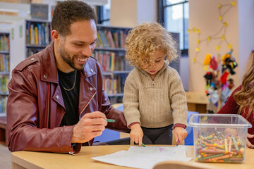 Adult male and young child engaged in drawing together with colorful crayons on paper in a public library, Cleveland, Ohio, USA