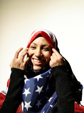 Smiling woman wearing a hijab with the American flag pattern touching her cheeks with a warm expression.
