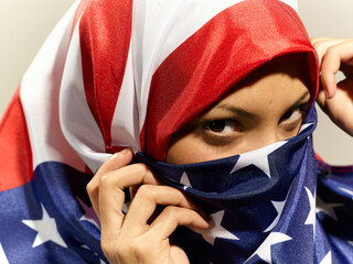 Woman with an American flag draped over her head, peeking out with one eye.