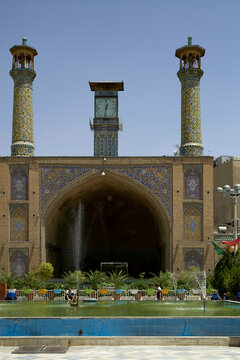 Majestic mosque with intricate blue tilework and twin minarets under a clear sky, fronted by a fountain and pool, Teheran, Iran