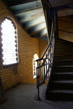 Spiral staircase winding up inside an empty vintage building with brick walls and a large arched window filtering in daylight, Berlin, Germany
