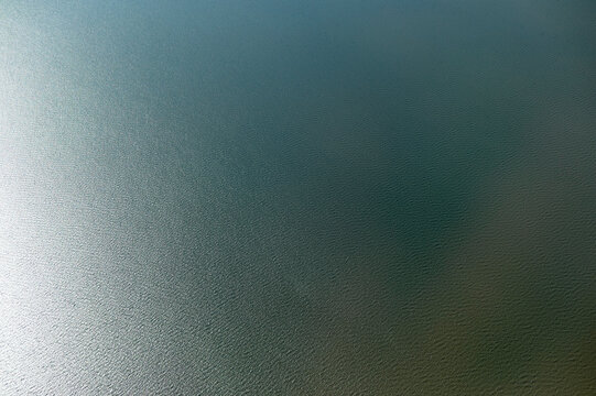 Aerial view shot from a plane of a calm, expansive body of water with a gradient of blue shades and gentle ripples on the surface, near New Orleans, USA