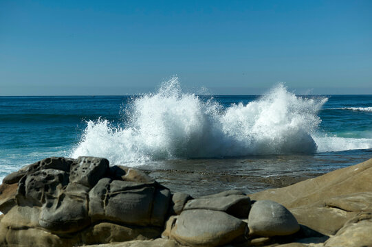 Ocean wave crashing against rocks with a clear blue sky, New Orleans, USA