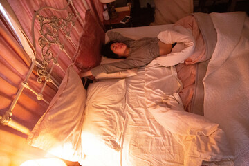Woman resting in a cozy bedroom with subdued lighting, Auckland, New Zealand