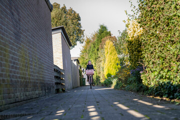 A person rides a bicycle down a sunny suburban alley flanked by houses and green hedges, Netherlands