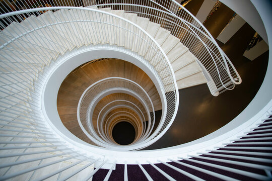 Spiral staircase with white balustrades descending into darkness, viewed from above in the university library of Helsinki (Helsingin yliopiston pääkirjasto Kaisa-talo)