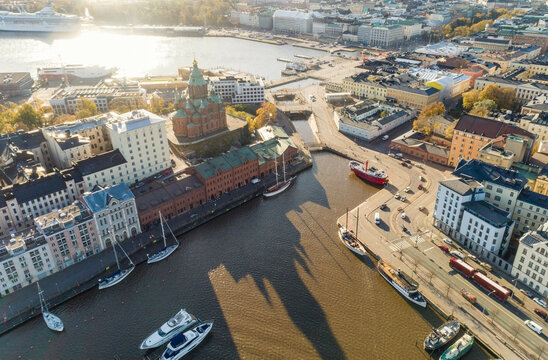 Aerial view of a sunlit urban coast with historical buildings in the heart of Helsinki, boats, and a waterfront promenade with Uspenski Cathedral, Finland