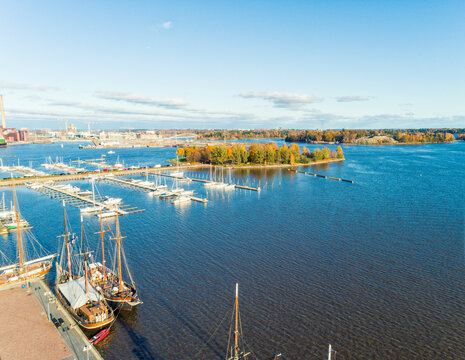 Aerial view of a marina with boats docked in neat rows, surrounded by autumn foliage and calm waters and Tervasaari island in Helsinki, with archipelago in the distance, Finland