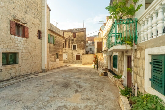 Cobblestone street flanked by traditional stone houses with colorful windows and balconies in a Mediterranean village of Ka?tel Gomilica in Kastela, Croatia at dusk or sunset
