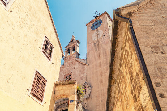 Historic buildings with shuttered windows flank narrow streets leading to an aged clock tower of Church of the Holy Spirit   in Omis under a clear blue sky, Croatia