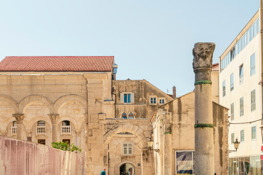 Ancient Roman column stands prominently in front of historical Church of St. Roch and Diocletian's Palace under a clear blue sky, Split, Croatia