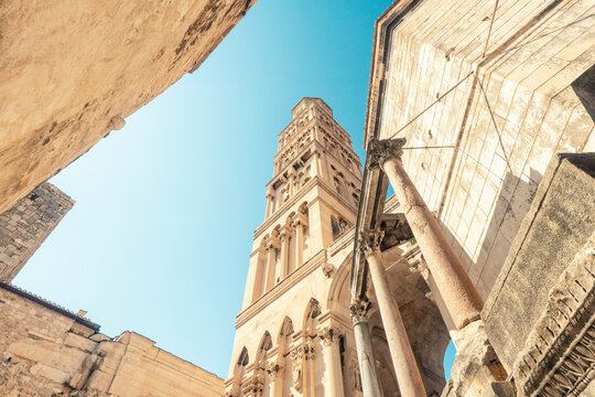 Bell tower of an ancient stone St Domnius cathedral rising into the clear blue sky, framed by old buildings on either side, Split, Croatia