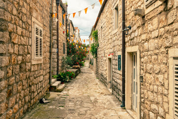 Cobblestone street with stone buildings and festive flags hung overhead in a historic old town, Mali Ston, Croatia
