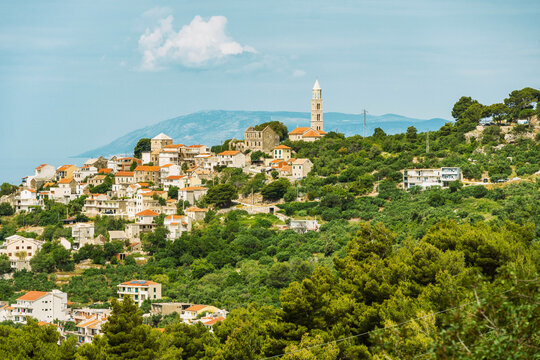 Hillside town of Igrane overlooking a lush green landscape with a prominent church tower and terracotta rooftops under a clear blue sky, Croatia