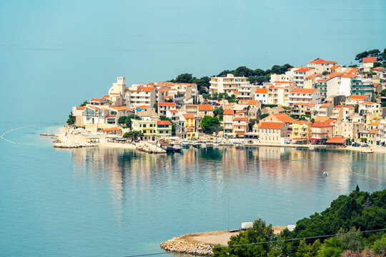 Coastal town of Igrane perched on a hillside by the sea with reflection on the water and a clear blue sky, Croatia