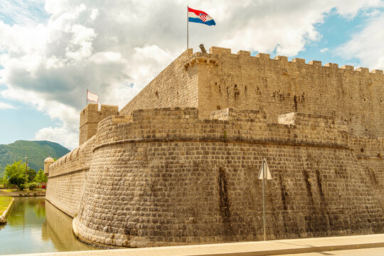 Medieval Kastio Fort with flags waving under a cloudy sky, surrounded by a moat, Ston, Croatia