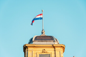 Croatian flag waving above an ornate gold-trimmed dome of Opera House Building against a clear blue sky in Zagreb, Croatia